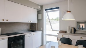 A modern kitchen with white cabinets, a black stove, and a dining area with a table and chairs. - 4 Person Holiday Home in Romo (Rømø)