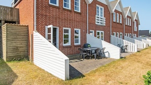 A row of red brick houses with white trim, a covered patio with a table and chairs, and a wooden fence. - 4 Person Holiday Home in Romo (Rømø)