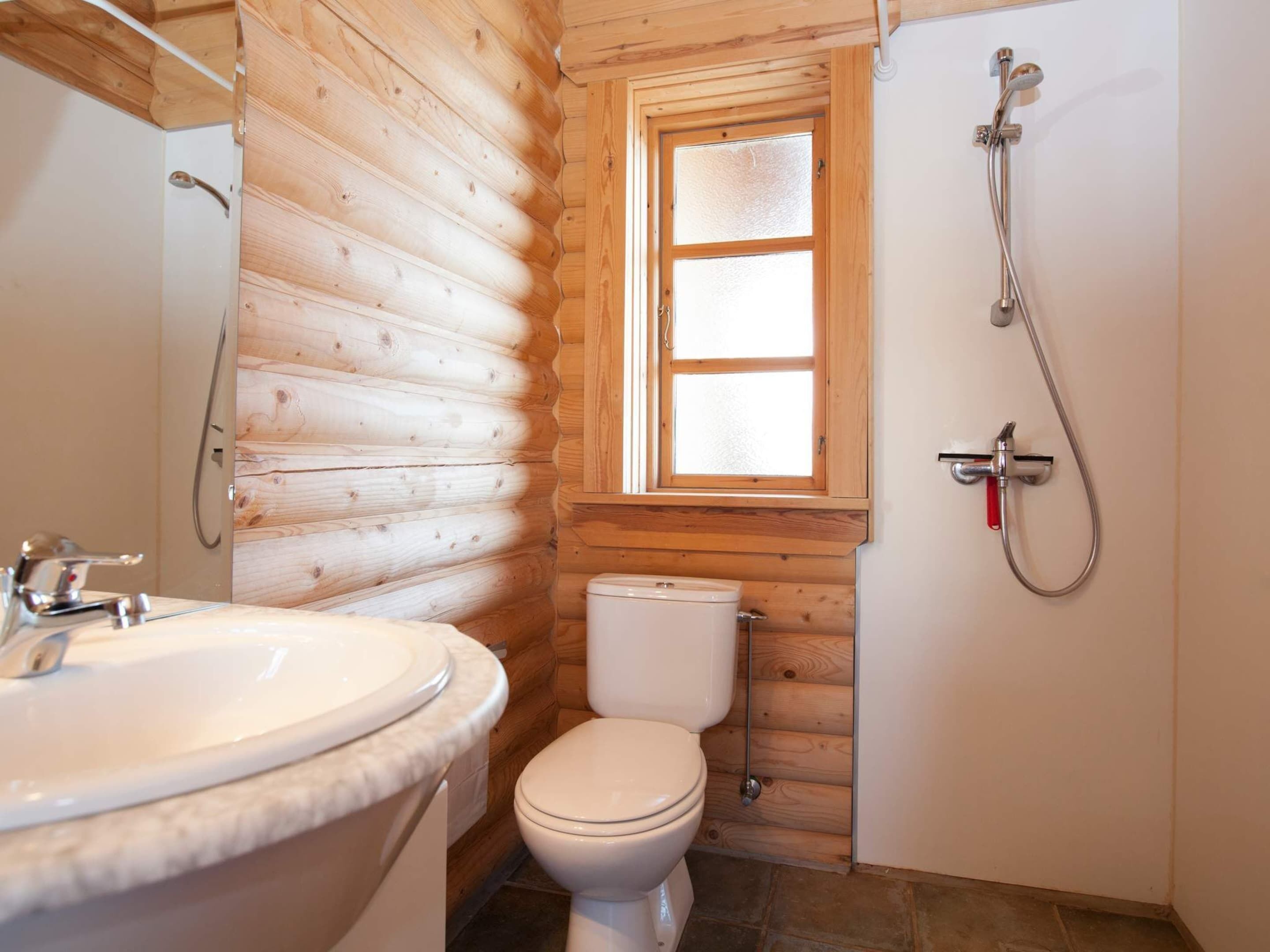 A bathroom with a wooden interior, a white sink, a toilet, and a shower.