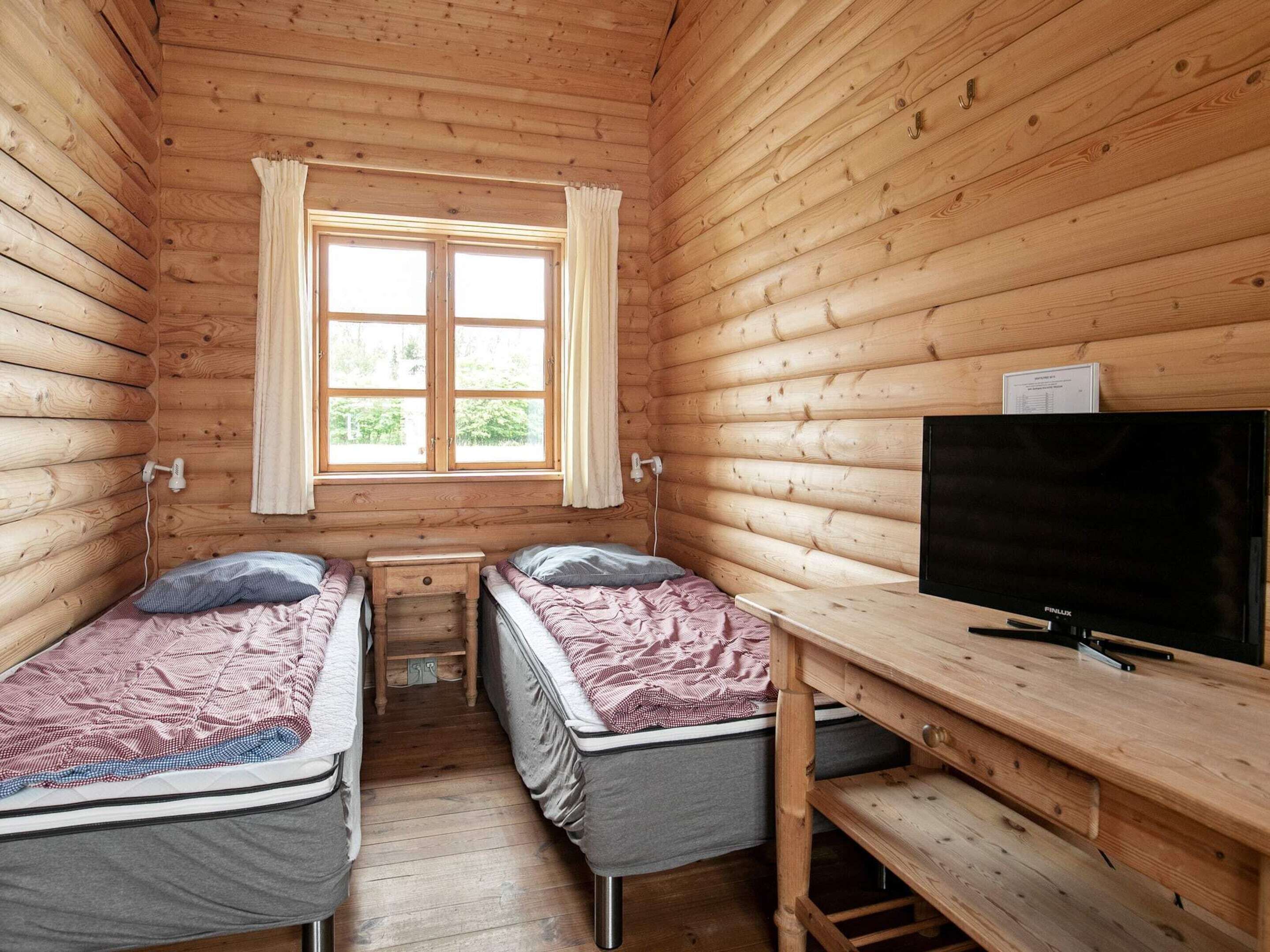 Uma cabana com duas camas, uma televisão e uma janela com cortinas.
