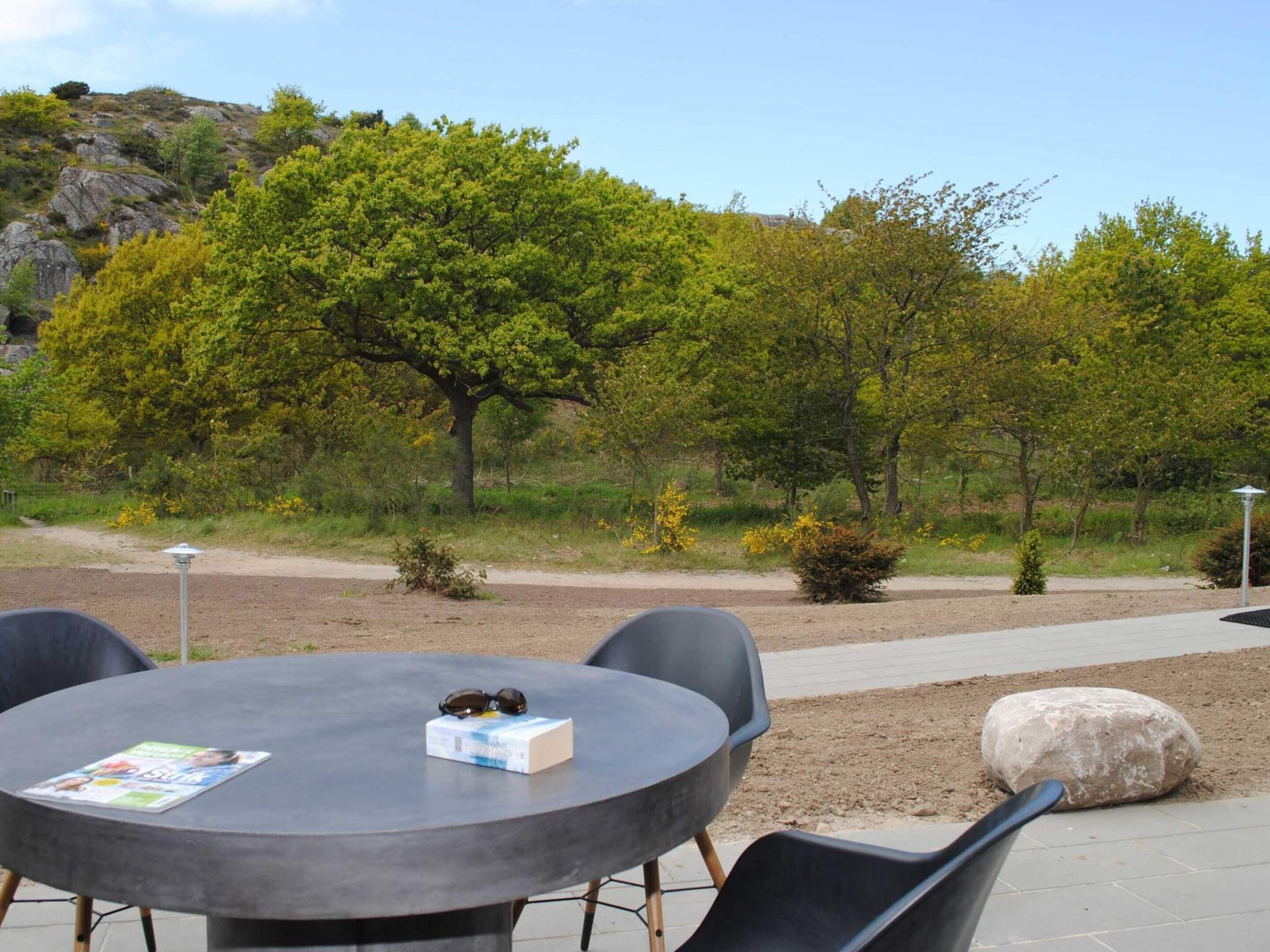 Un espace extérieur aménagé avec une table ronde et des chaises, entouré d’arbres et bordé d’un sentier de terre.
