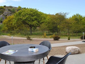 An outdoor seating area with a round table and chairs, surrounded by trees and a dirt path. - 4 Person Holiday Home in Allinge (Allinge)