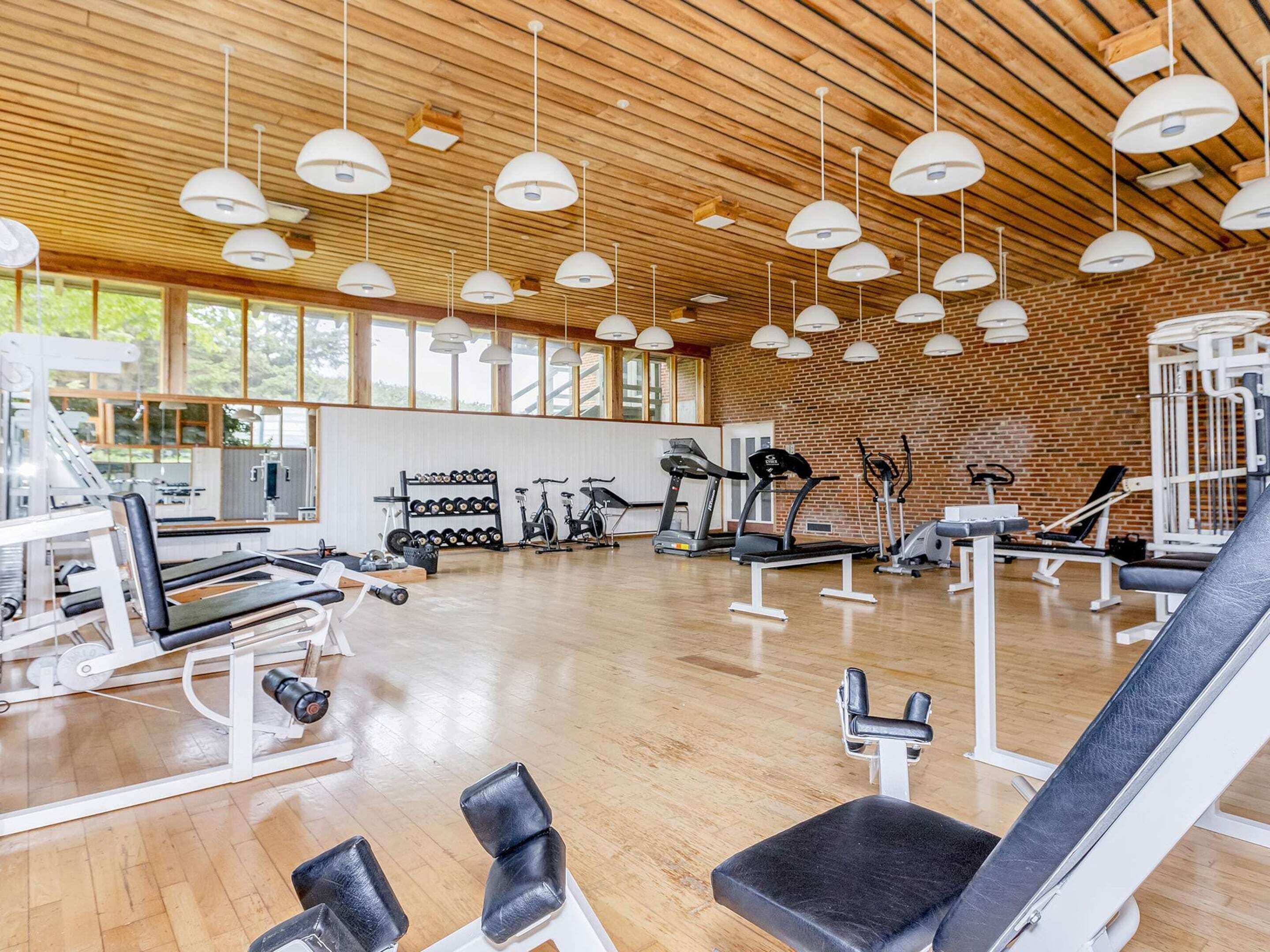 Une salle de sport spacieuse, dotée de divers appareils d’exercice, de grandes fenêtres et d’un plafond en bois.