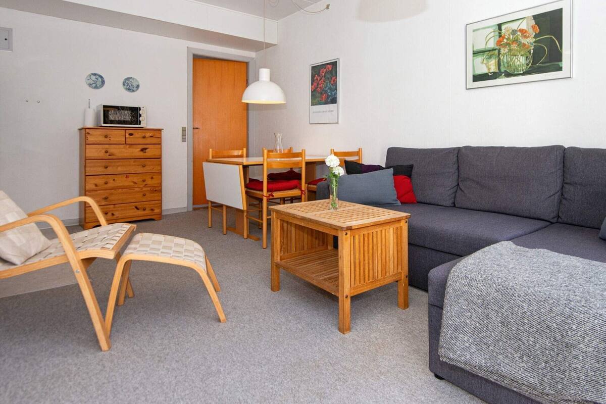 Un espace de vie compact comprenant un canapé, une table en bois, une chaise, une commode et une table à manger.