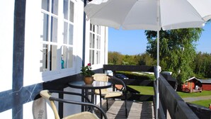 Een terras met een tafel, stoelen, een witte parasol en uitzicht op de omgeving.