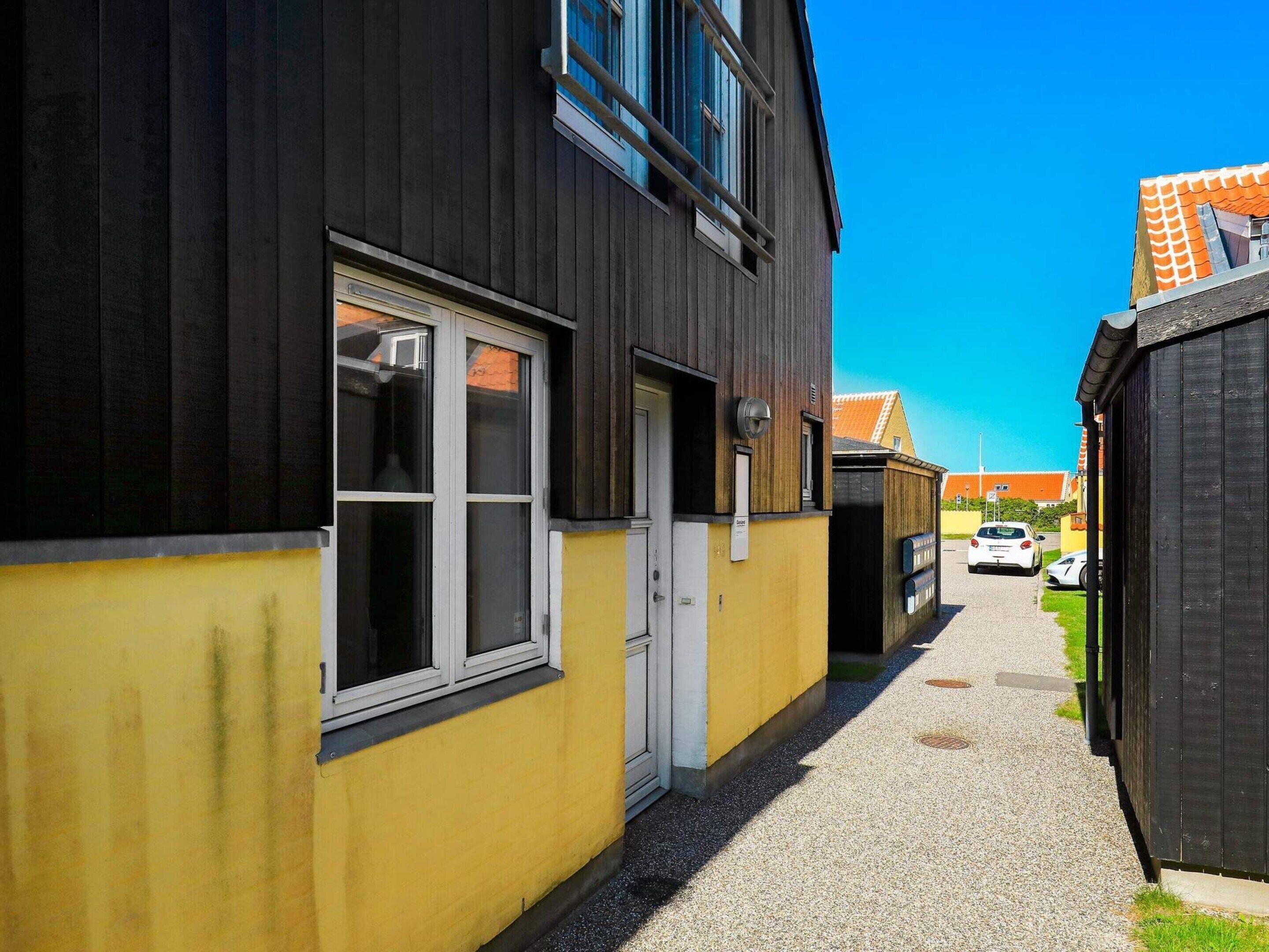 A narrow alleyway with a building on the left painted in dark and yellow, a door, and windows.