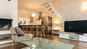 Una sala de estar moderna con una mesa de centro de vidrio, televisor, chimenea, comedor y una escalera.