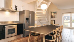 Una cocina moderna con horno empotrado, refrigerador de acero inoxidable y una mesa de comedor de madera con sillas.