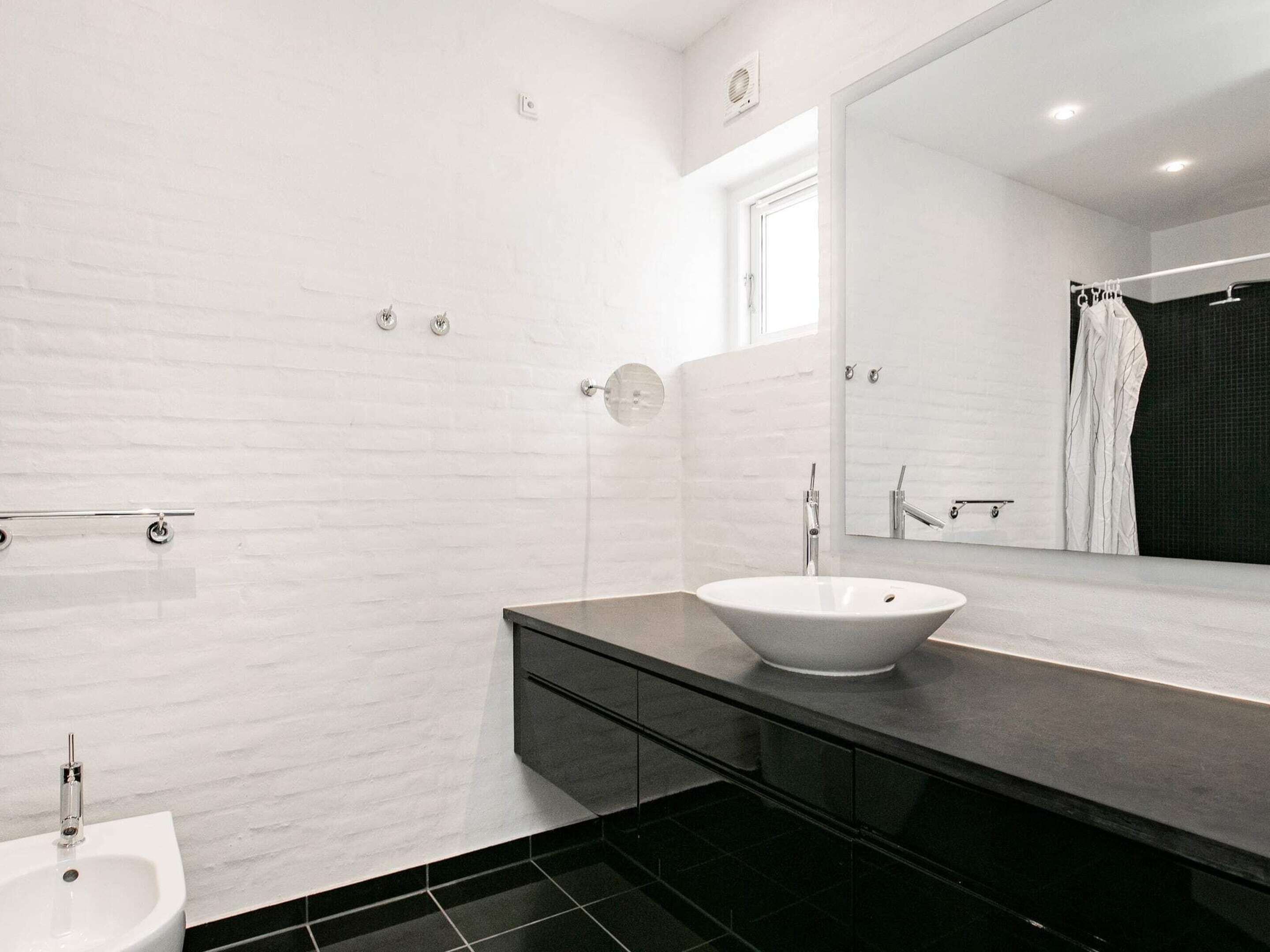 Une salle de bain moderne avec un lavabo blanc, un grand miroir et un plan de toilette foncé.
