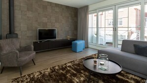 Un soggiorno moderno con una TV a schermo piatto, un divano, un tavolino da caffè e un'ampia finestra che offre vista sugli edifici circostanti.