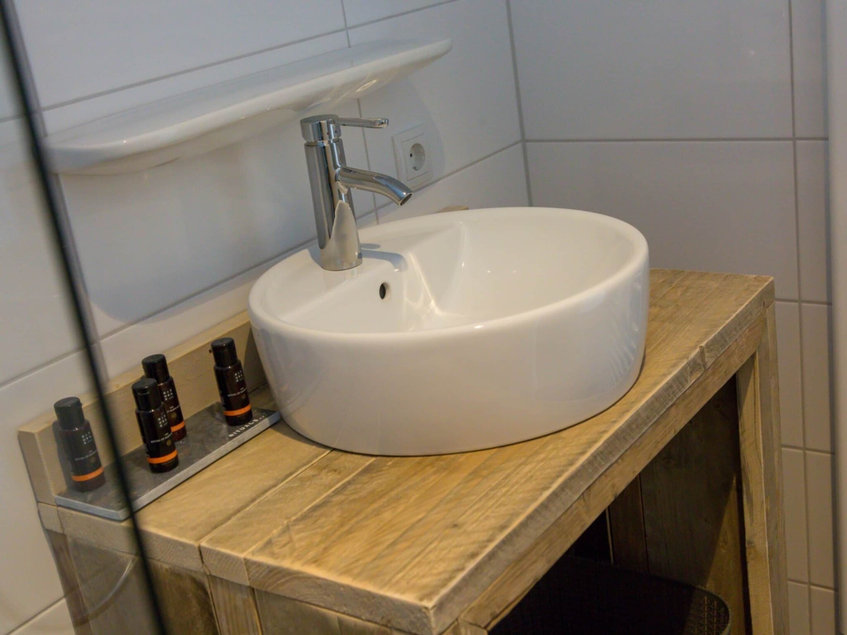 Un baño con lavamanos blanco, tocador de madera y espejo.