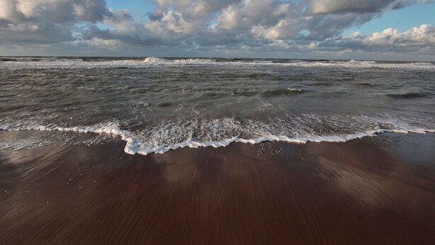 Una spiaggia con le onde che si infrangono sulla riva, sotto un cielo parzialmente nuvoloso.