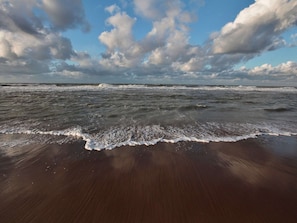 Ein Strand mit an die Küste rollenden Wellen unter einem teils bewölkten Himmel.