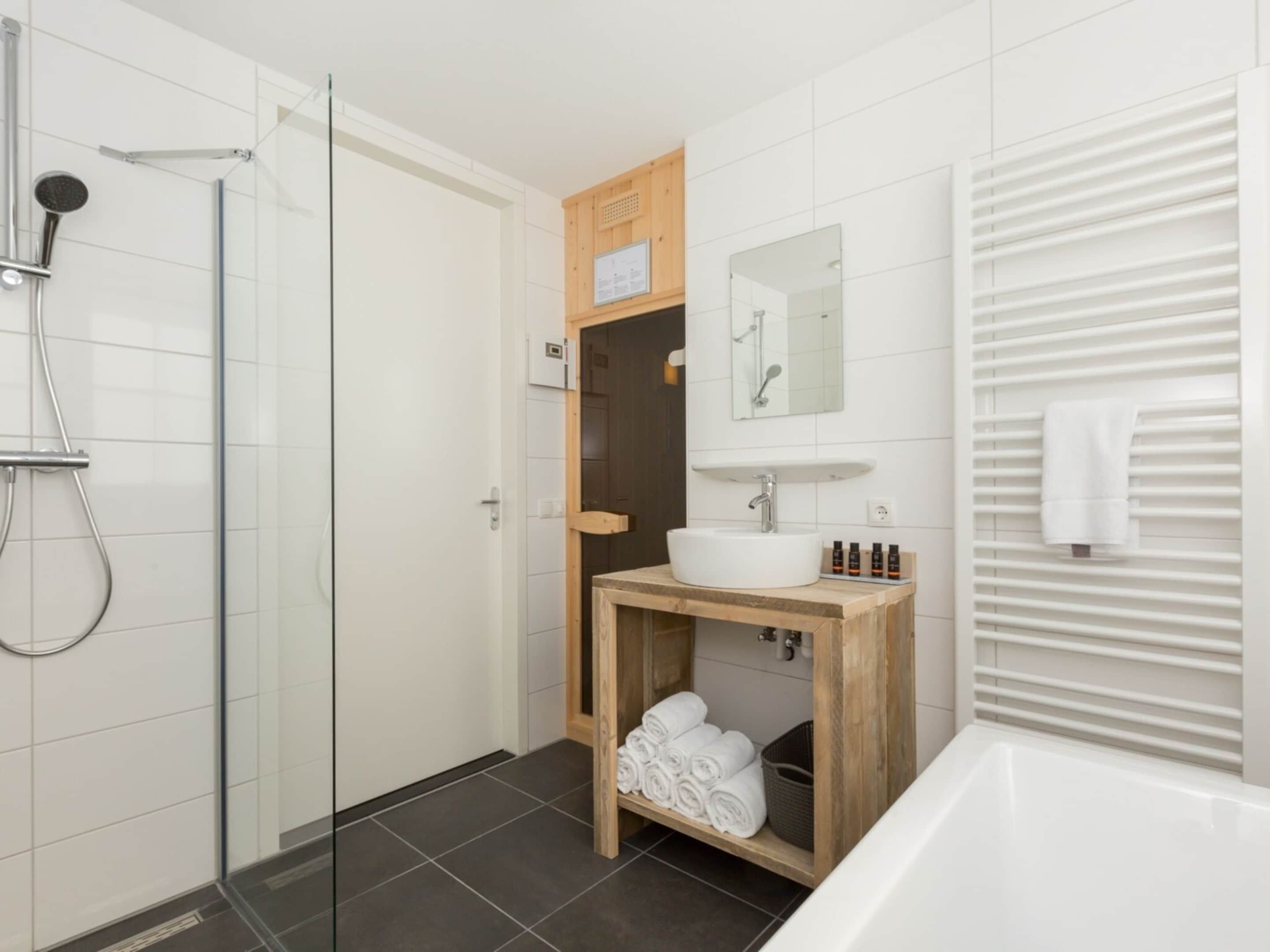 Un baño moderno con cabina de ducha de vidrio, tocador de madera con lavabo y espejo, y una bañera blanca.