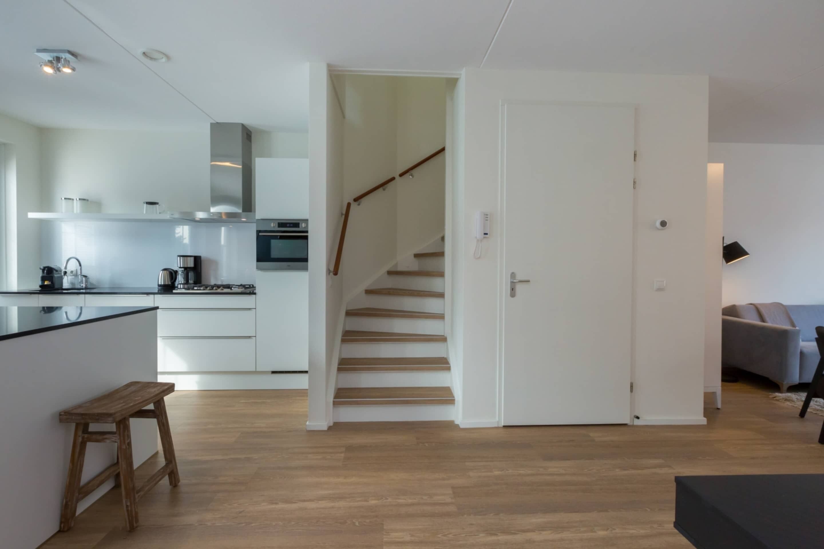 Eine moderne Küche mit weißen Schränken, einer Holzbank und einer Treppe, die in einen anderen Raum führt.