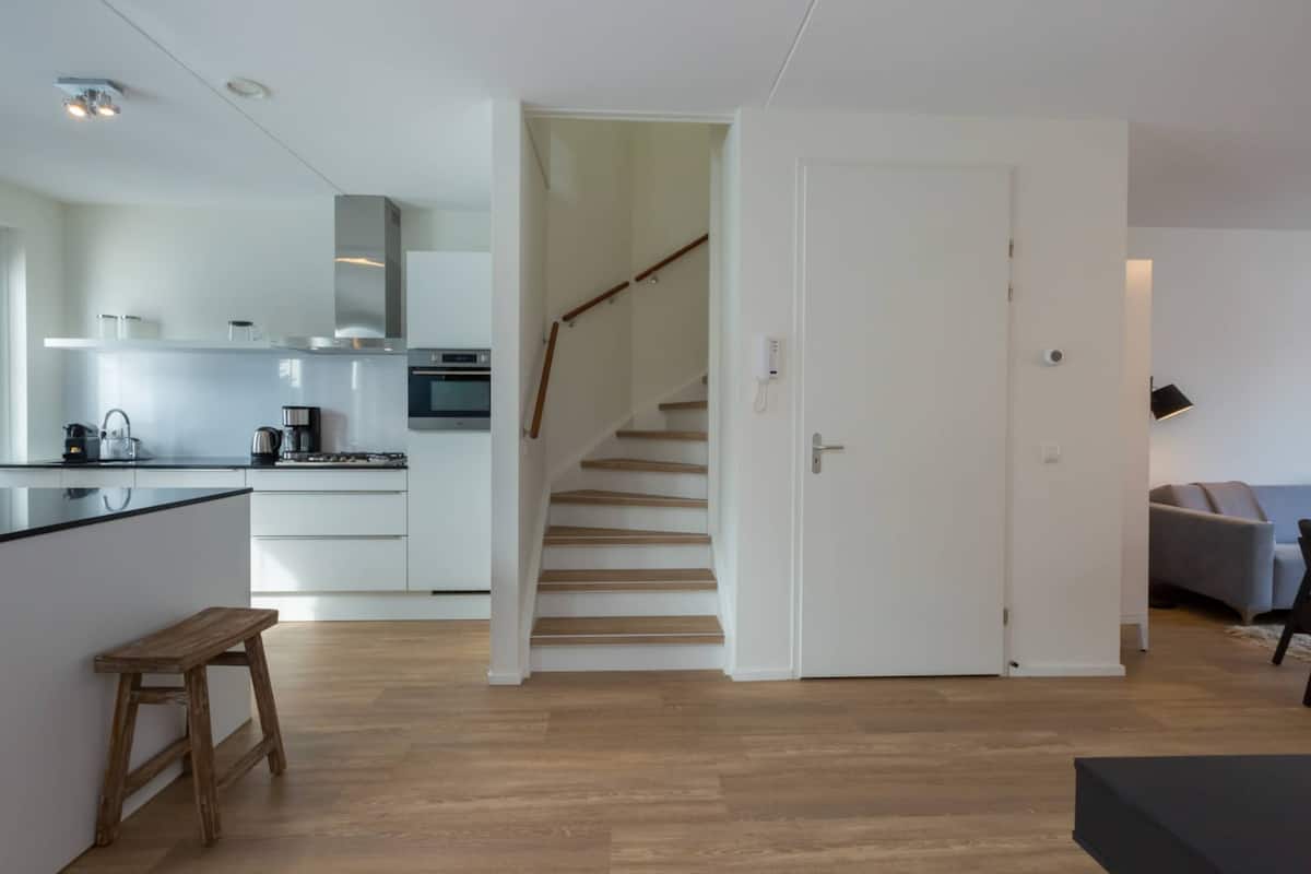 A modern kitchen with white cabinets, a wooden bench, and a staircase leading to another room.
