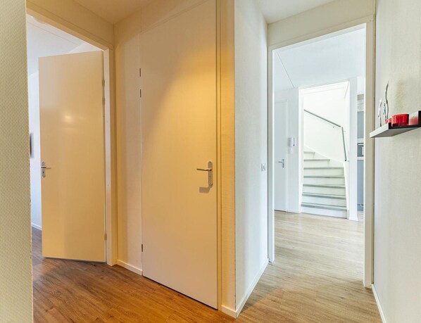 A hallway with wooden flooring, white walls, and a staircase leading to an upper level. - Luxury Apartment With Sauna the Foot of the Dunes (Koudekerke)