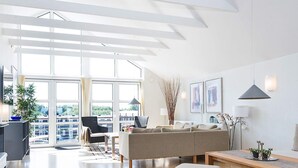 Een moderne woonkamer met een bank, stoelen, een salontafel en uitzicht door grote ramen.
