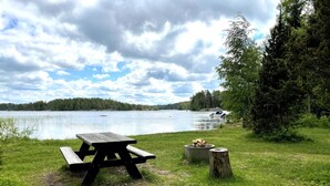 Un tavolo da picnic con un braciere, una zona erbosa e un lago con barche sullo sfondo.