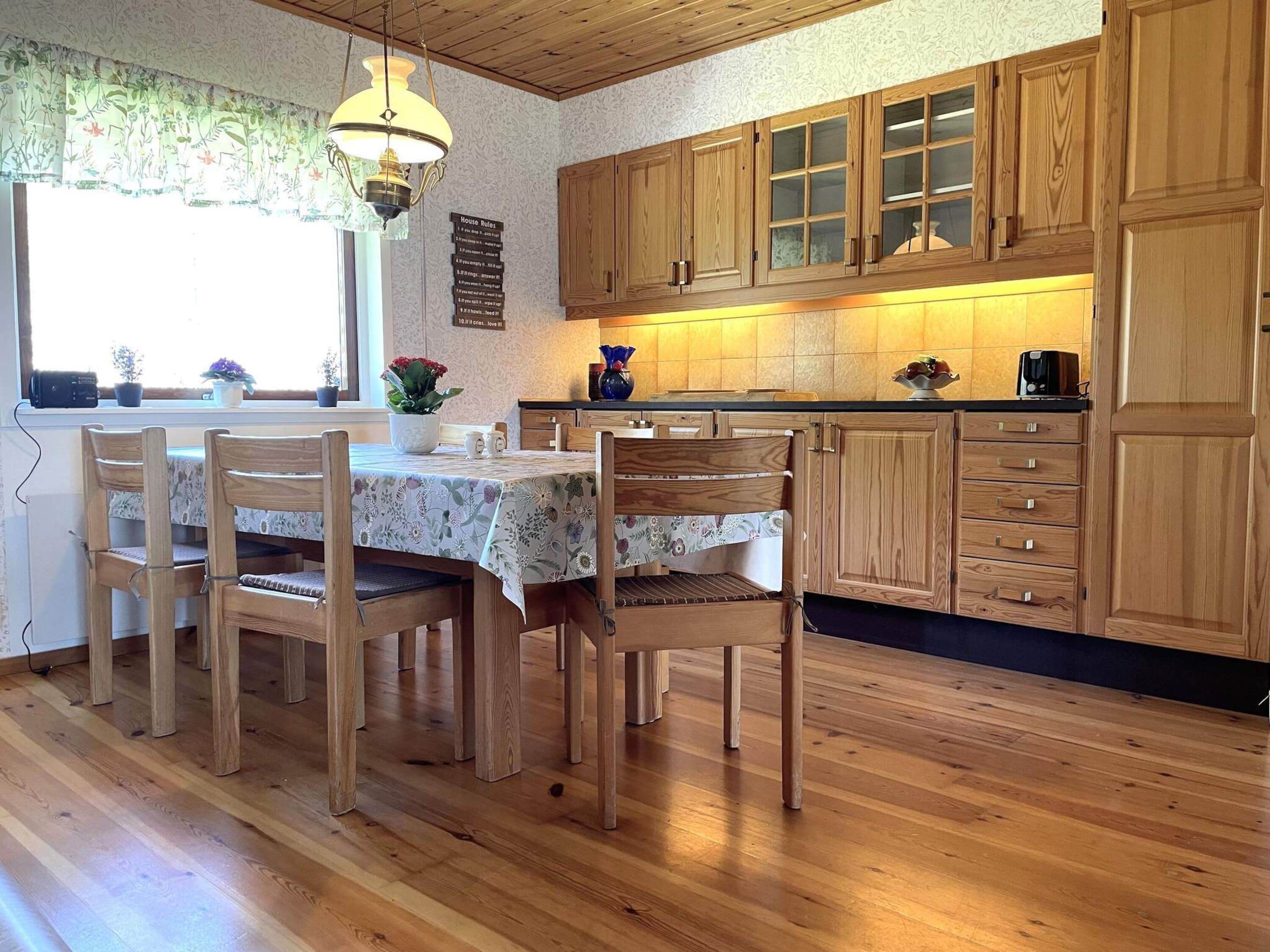 A kitchen with wooden cabinets, a dining table with chairs, and a hanging light fixture.