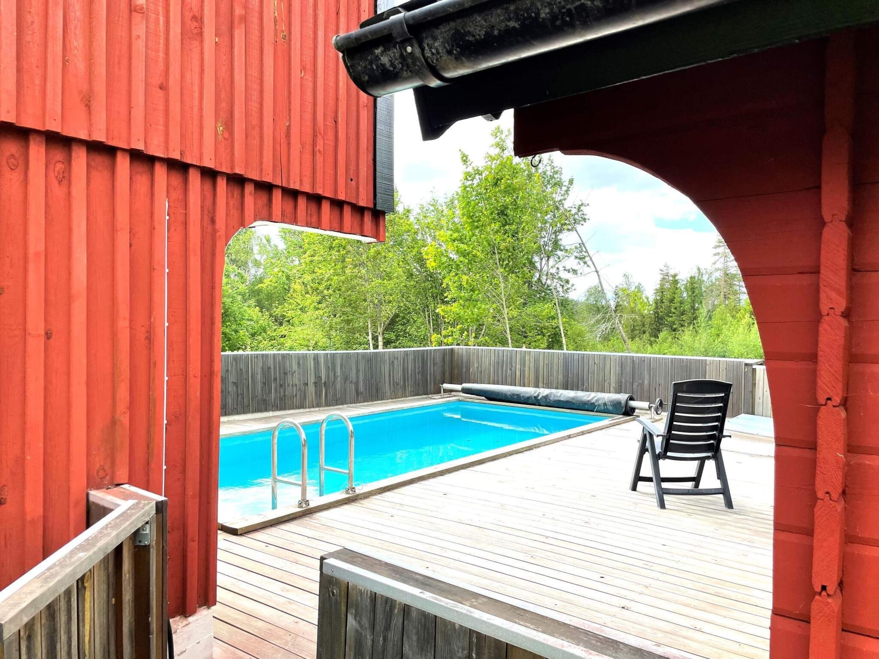 A wooden deck with a swimming pool, a covered area, and a chair.