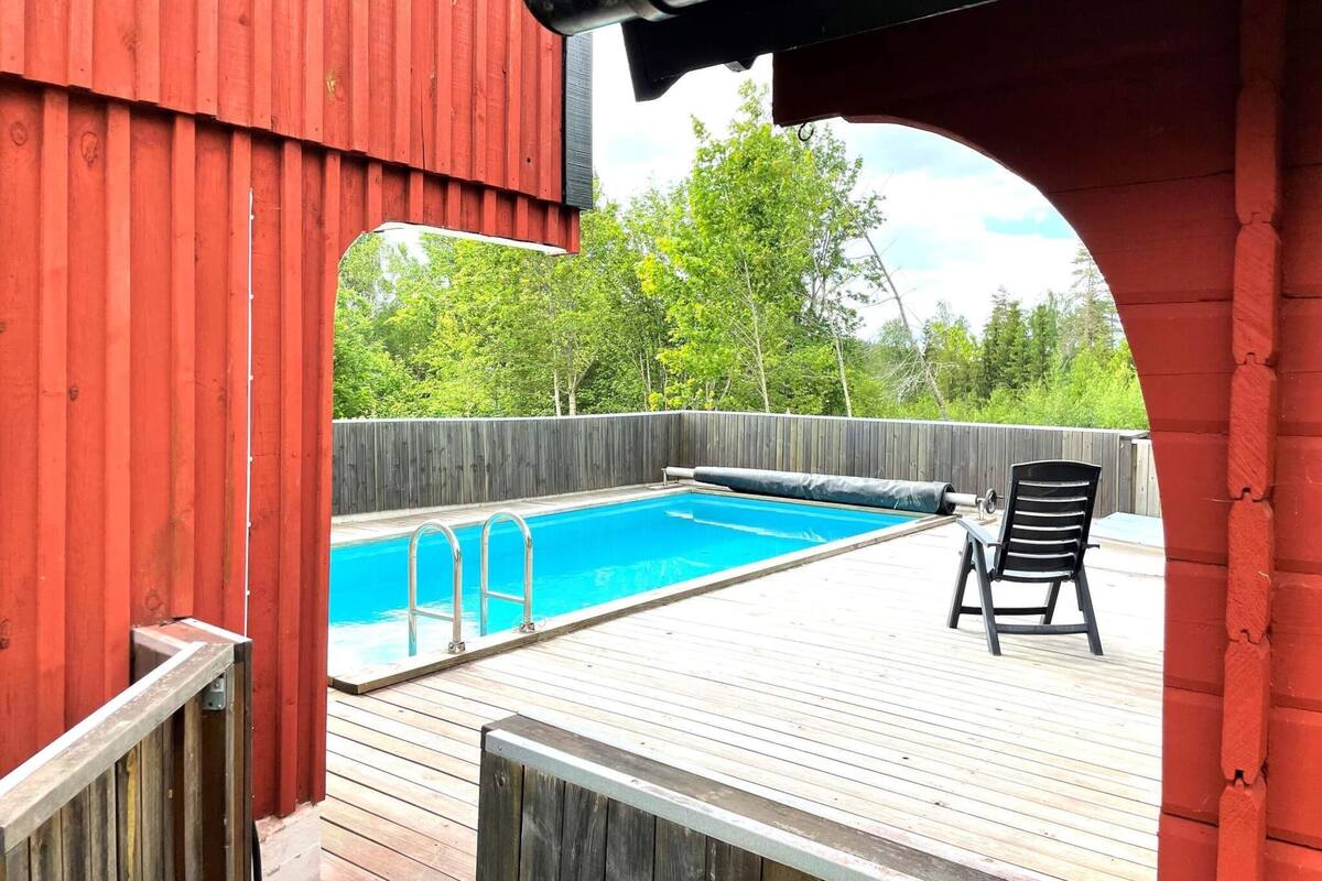 A wooden deck with a swimming pool, a covered area, and a chair.
