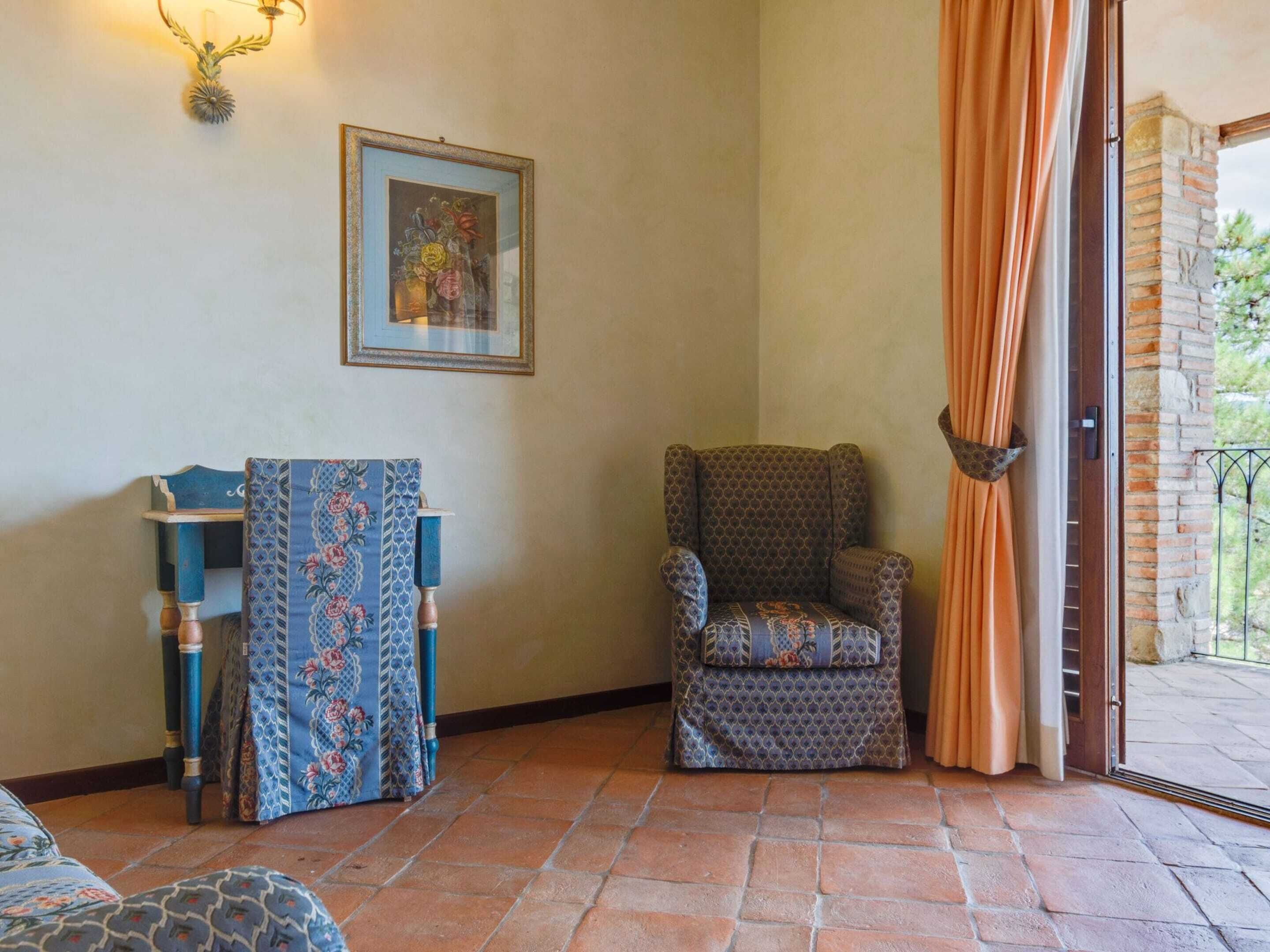 A corner room with a patterned armchair, a blue armchair with floral upholstery, and a framed artwork on the wall.