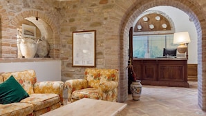 A stone-walled room with a reception desk, a sofa, and a table. - Elegant Apartments in Resort With Swimming Pool set in Nature (Collazzone)
