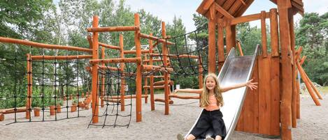 Un parque infantil con tobogán, estructuras de escalada y una casita de madera.