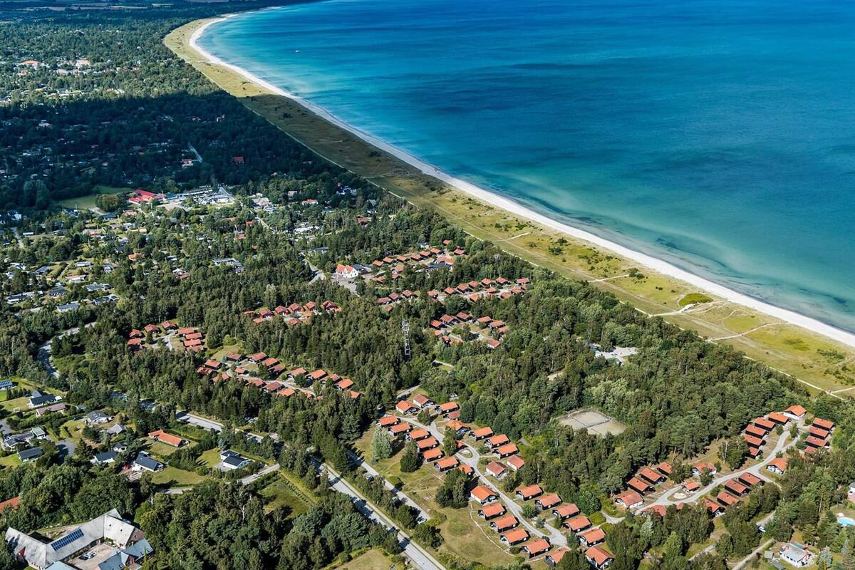 Vue aérienne d’un quartier résidentiel situé sur la côte, où les maisons sont disposées en forme de demi-cercle autour d’une plage.