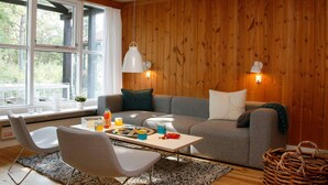 A cozy living room with a wooden wall, a grey sofa, a white armchair, and a small table with drinks and snacks. - 6 Person Holiday Home on a Holiday Park in Vaeggerlose (Vaeggerlose)