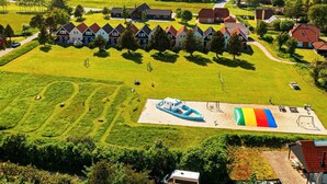 A residential area with multiple houses, a large grassy field, and a playground with a slide and swings. - 10 Person Holiday Home on a Holiday Park in Blavand (Blavand)