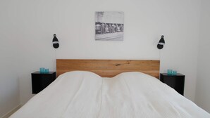 Een slaapkamer met een houten hoofdbord, een wit sprei, twee nachtkastjes met lampen en een zwart-wit foto aan de muur.