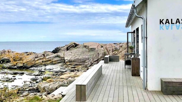 Een gebouw aan de kust met een houten terras, met uitzicht op rotsachtig terrein en de zee.
