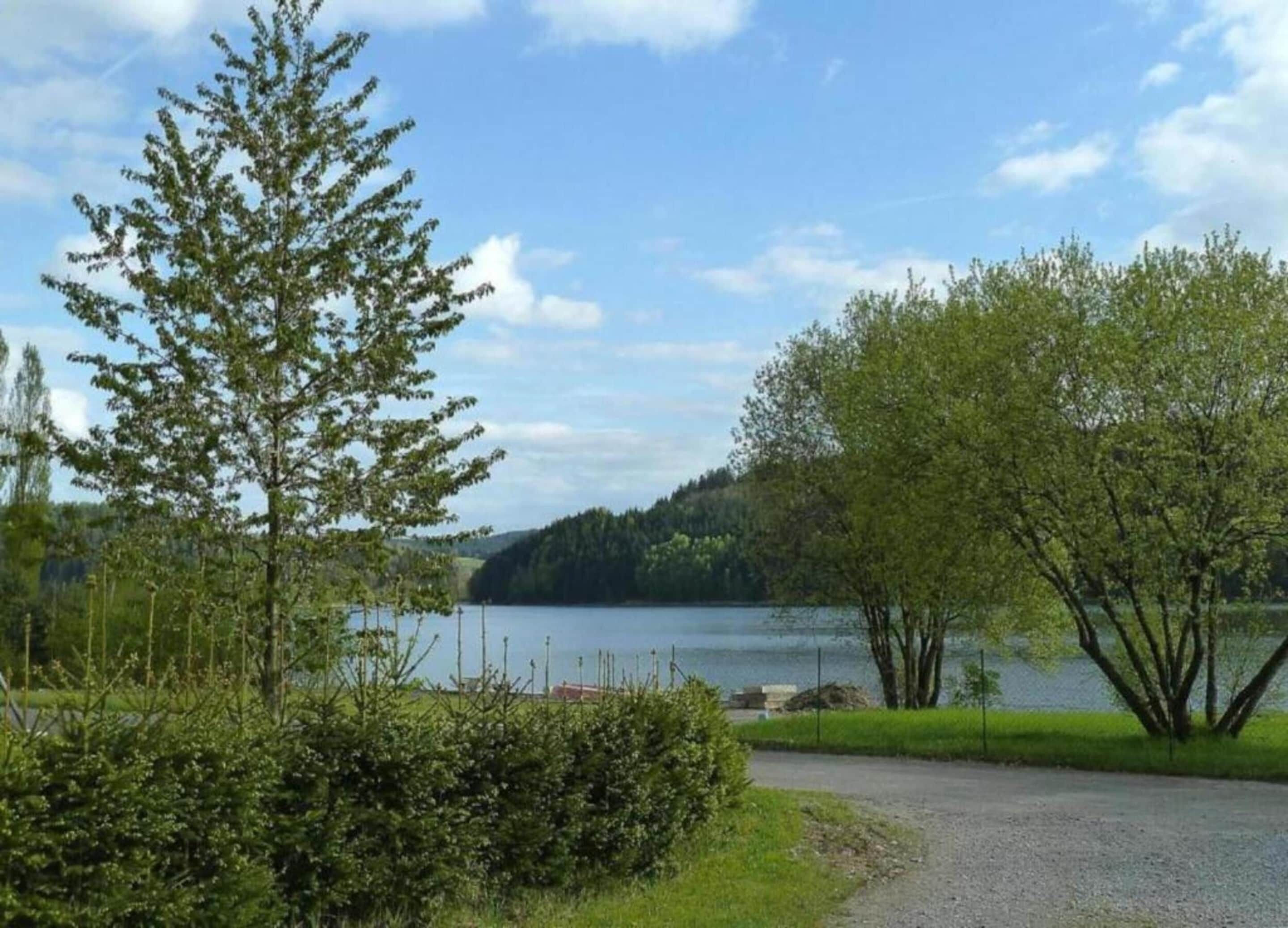 A gravel path leading to a lake with trees and a distant hill.