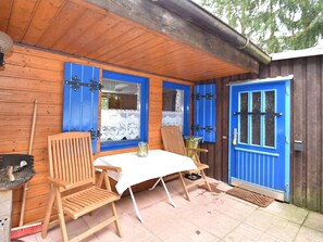 Une cabane en bois avec un coin repas comprenant une table et deux chaises, une porte bleue et une fenêtre ornée de rideaux en dentelle.