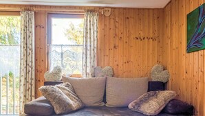 A cozy living room with a wooden wall, a sofa with fluffy cushions, and a glass coffee table with decorative items. - Comely Holiday Home in Guntersberge Near Forest (Harzgerode)