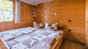 A cozy wooden cabin bedroom with a large bed, a window with curtains, and a small shelf. - Comely Holiday Home in Guntersberge Near Forest (Harzgerode)