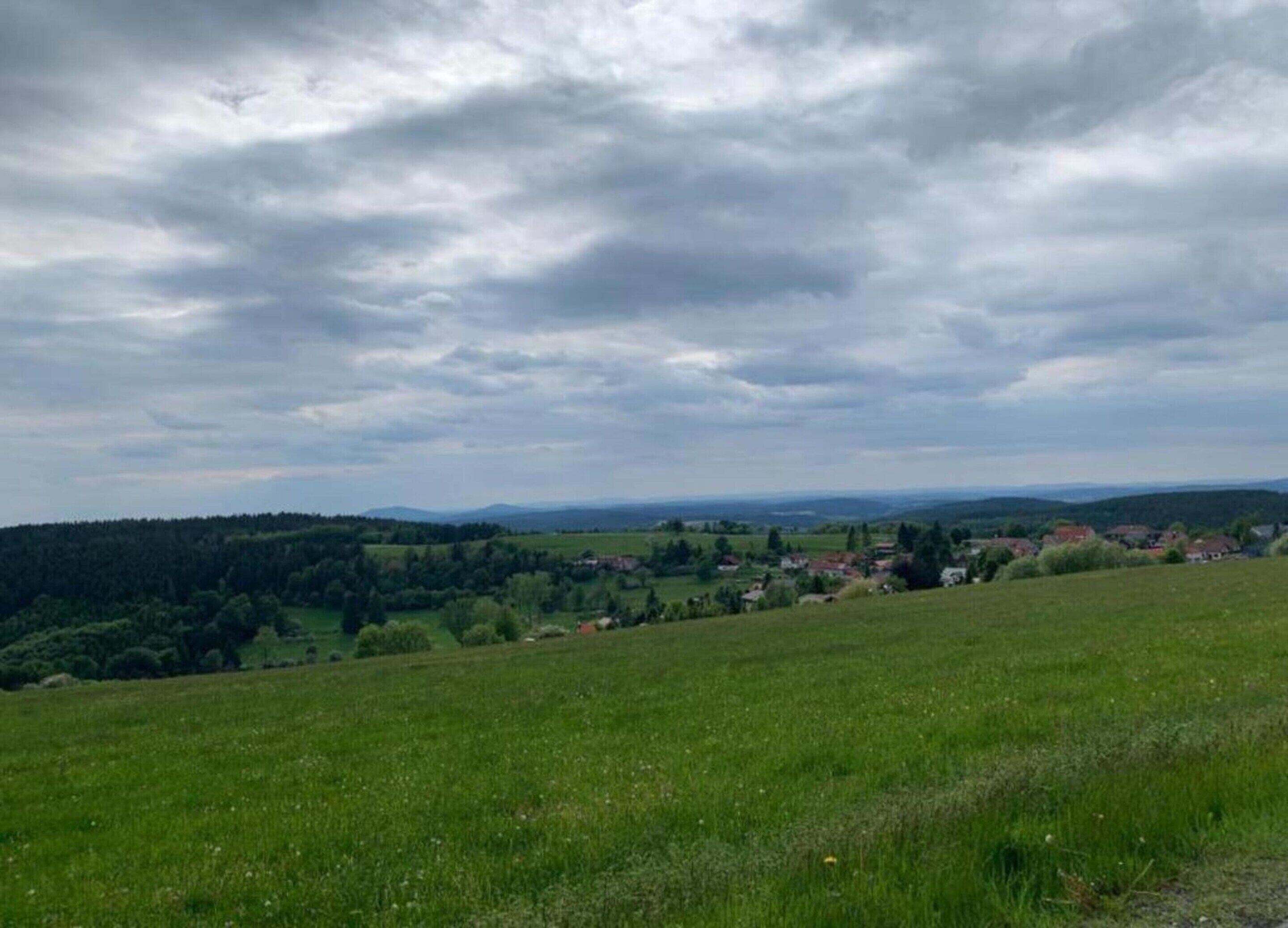 A panoramic view of a rural landscape with rolling hills, a small village, and a forested area.