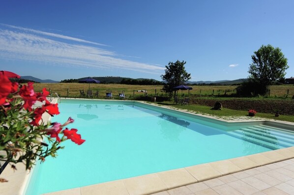 A swimming pool with lounge chairs and umbrellas, surrounded by a grassy area and trees. - Stunning Farmhouse in Passignano With Pool (Passignano sul Trasimeno)
