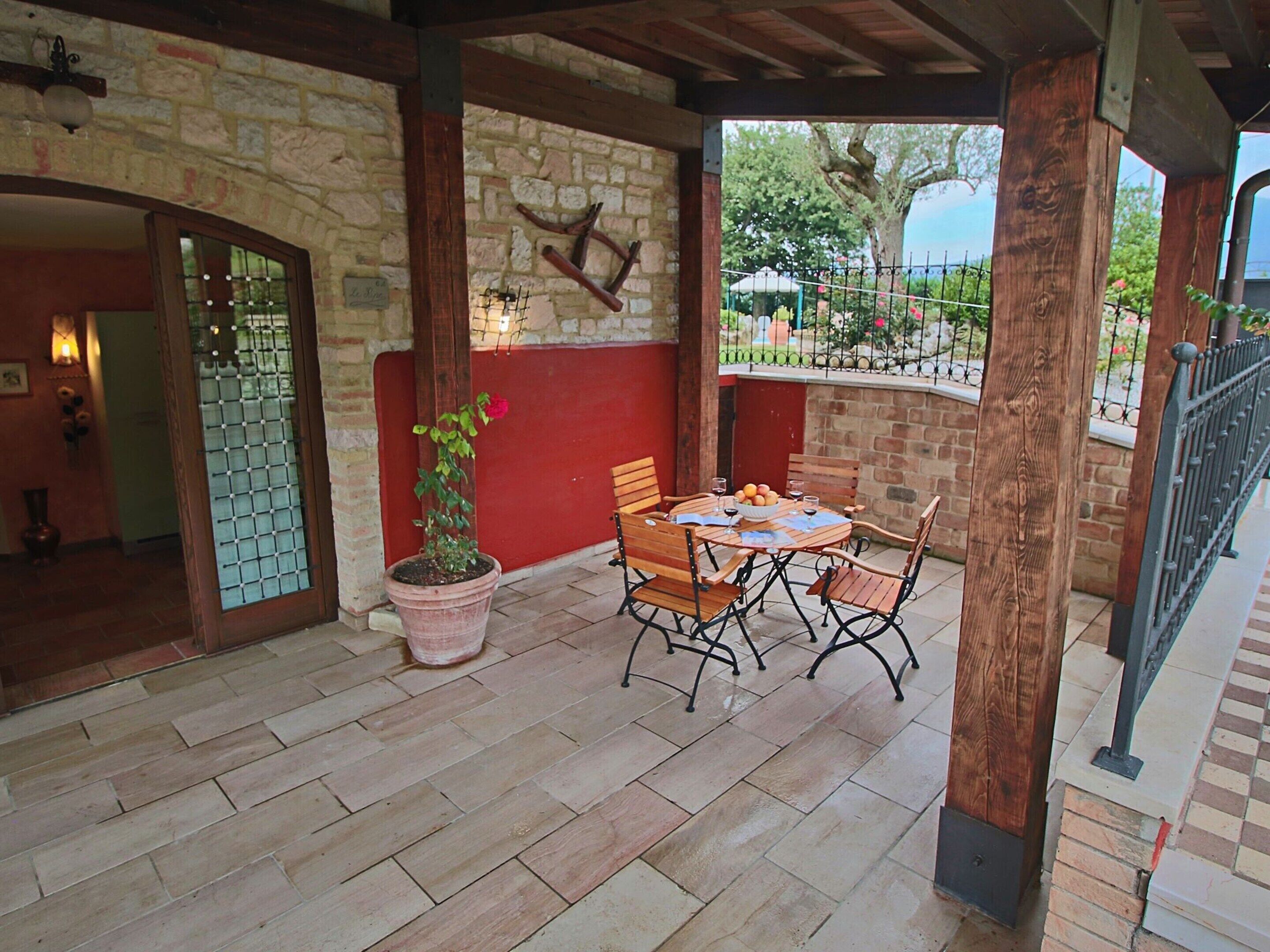 A covered patio with a stone wall, wooden table, and chairs.