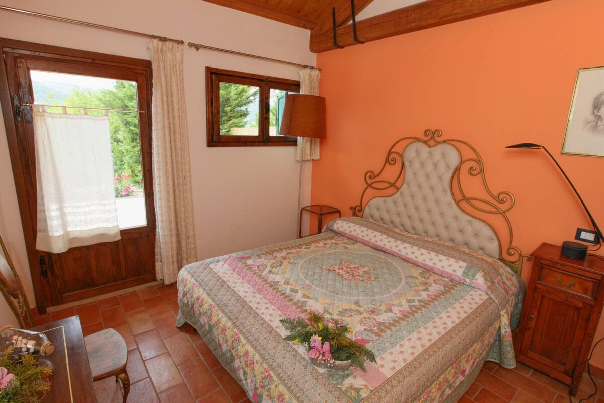 A bedroom with a large bed, a wooden door, a window, and a bedside table.
