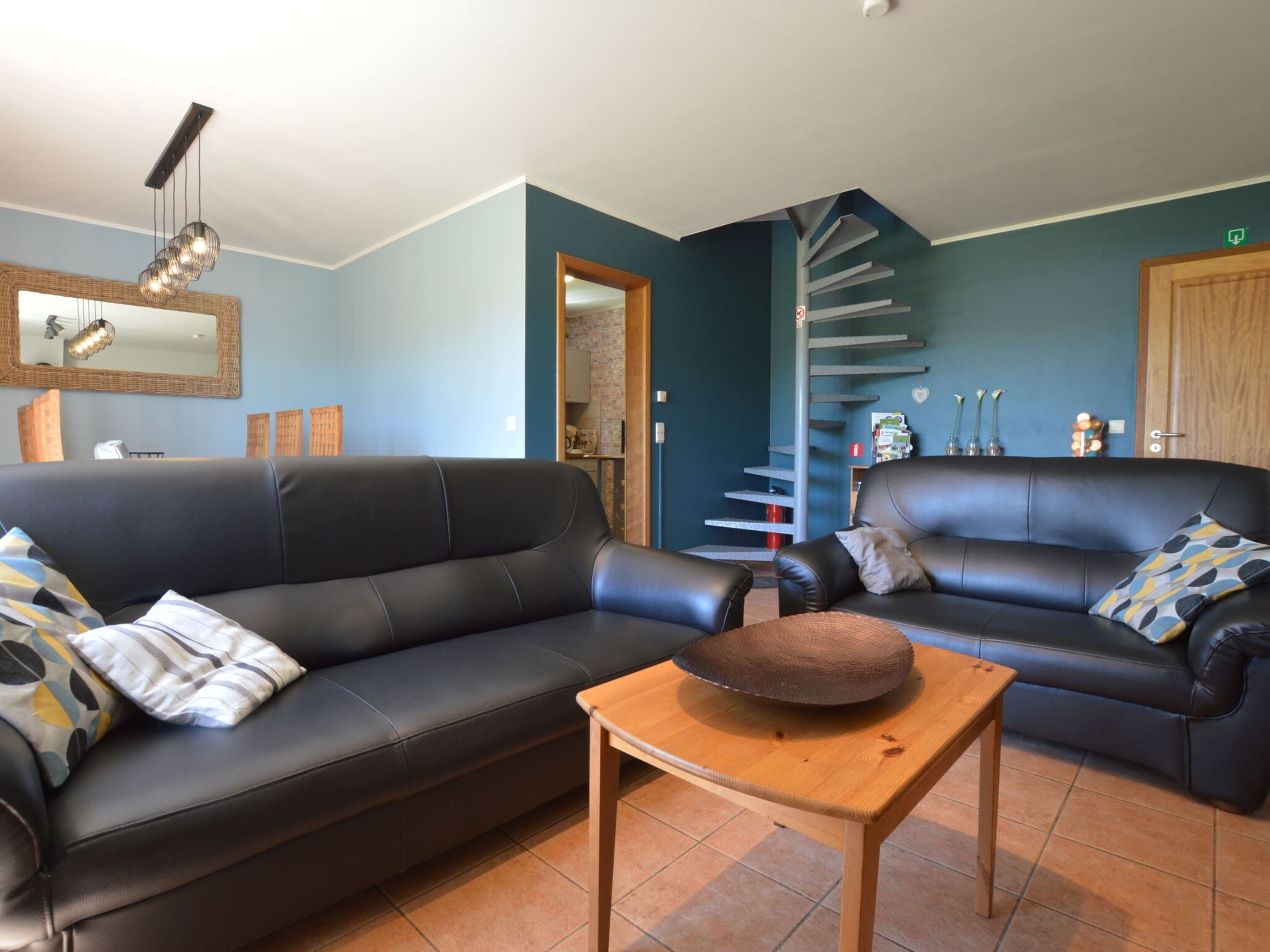 A living room with two black leather sofas, a wooden coffee table, and a spiral staircase in the background.