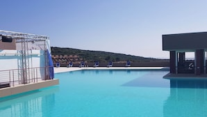 A clear blue swimming pool with a diving platform and lounge chairs. - Simplistic Apartment in Olbia With Garden (Olbia)