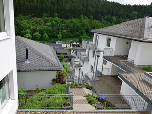 Un edificio de varios pisos con terraza en la azotea, zona de recepción y vistas a una ladera boscosa.