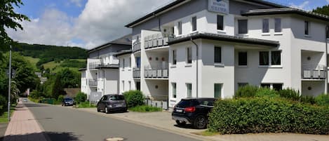 A multi-story residential building with balconies, a clear sky, and parked cars.