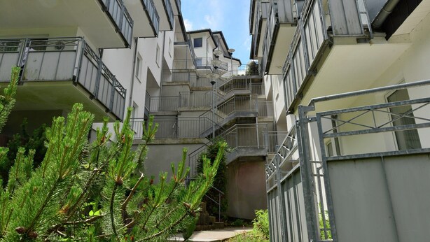 A multi-story residential building with balconies, staircases, and a small garden area with pine trees. - Holiday Home in the Centre of Willingen With View (Willingen)