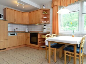 Une cuisine avec des meubles de rangement en bois, une table à manger avec des chaises et une fenêtre avec des rideaux.