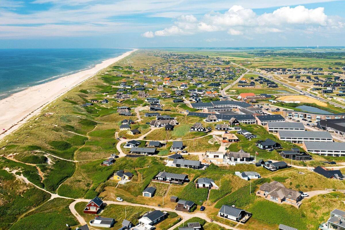 Une zone résidentielle côtière, avec des maisons construites sur un terrain herbeux, une plage et une vue lointaine sur la mer.