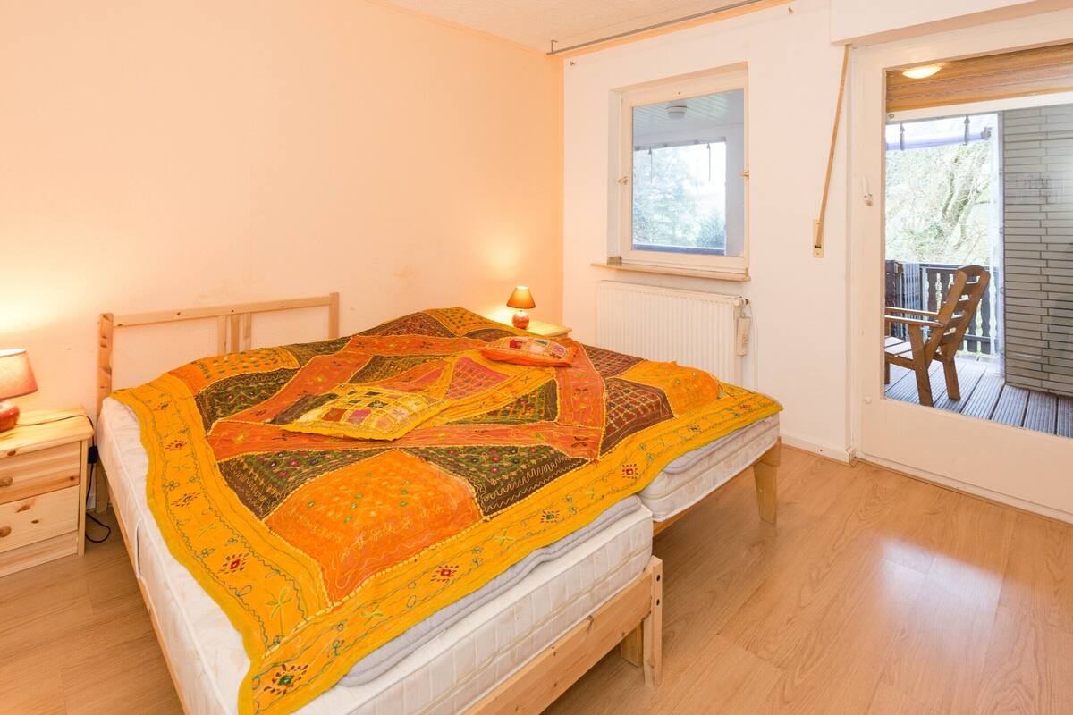 A bedroom with a wooden bed, a nightstand, a window, and a view of the outside deck.